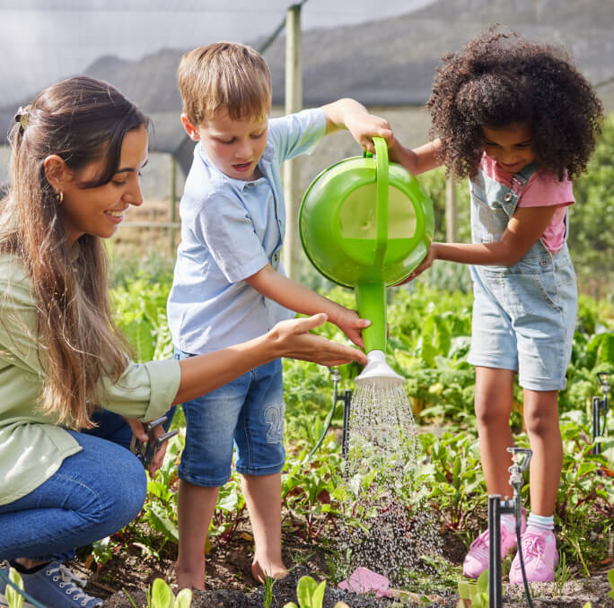 A woman and two children watering plants